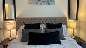 Habitación de hotel con cabecera capitonada, dos lámparas de noche, una obra de arte floral grande y un espejo en la pared.
