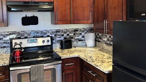 Una cocina con armarios de madera, estufa de acero inoxidable, refrigerador negro y microondas.