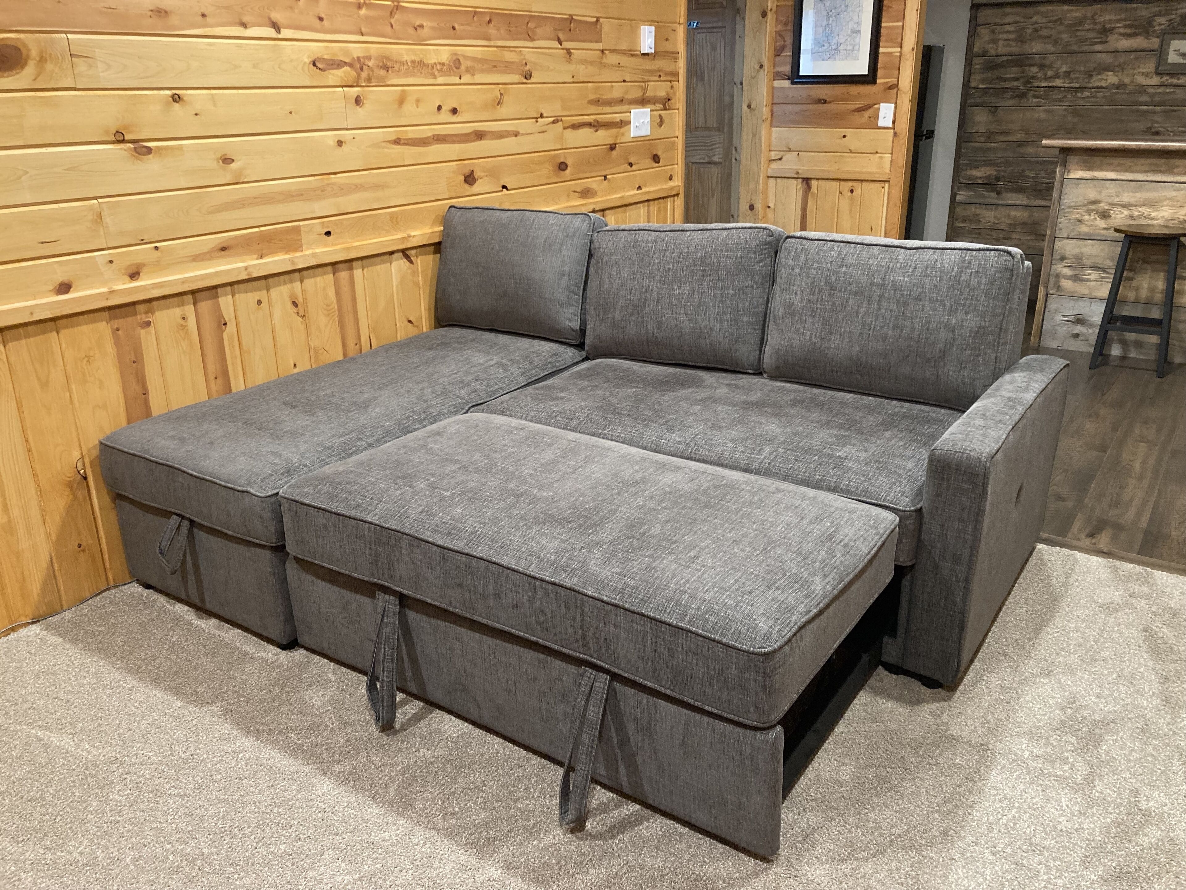 A grey sectional sofa with storage drawers against a wooden paneled wall.