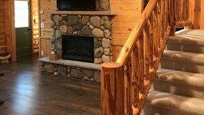 Un interior de madera con chimenea de piedra, un televisor montado sobre ella y una escalera con barandilla de madera.