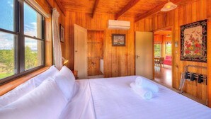 A wooden room with a bed, a window, and a door leading to another room. - Swan Cove (Coles Bay)