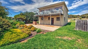 A modern two-story house with a balcony, surrounded by a well-maintained garden and a wooden fence. - Swan Cove (Coles Bay)