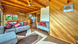 A spacious living room with a wooden ceiling, a gray sofa set, and a kitchen in the background. - Swan Cove (Coles Bay)