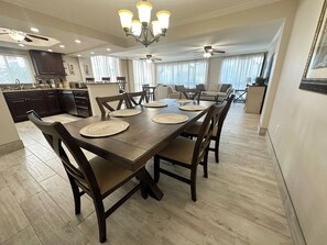 Un vaste espace dédié à la salle à manger, avec une table et des chaises en bois, un lustre et un ventilateur de plafond.
