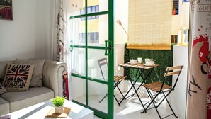A cozy living room with a green-framed sliding glass door, a sofa with a Union Jack pillow, a small table with a plant, and a view of the city through the window. - Casa Tiago With High-speed Wifi and Smart-tvv (La Oliva)