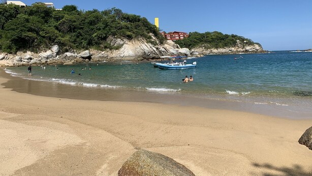 Una playa con agua cristalina, un bote y acantilados rocosos.