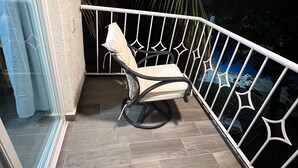 Un balcón con una silla acolchada, barandal blanco y vistas al cielo nocturno.