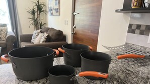 Una encimera de granito con cuatro ollas y sartenes negras, algunas con asas anaranjadas.