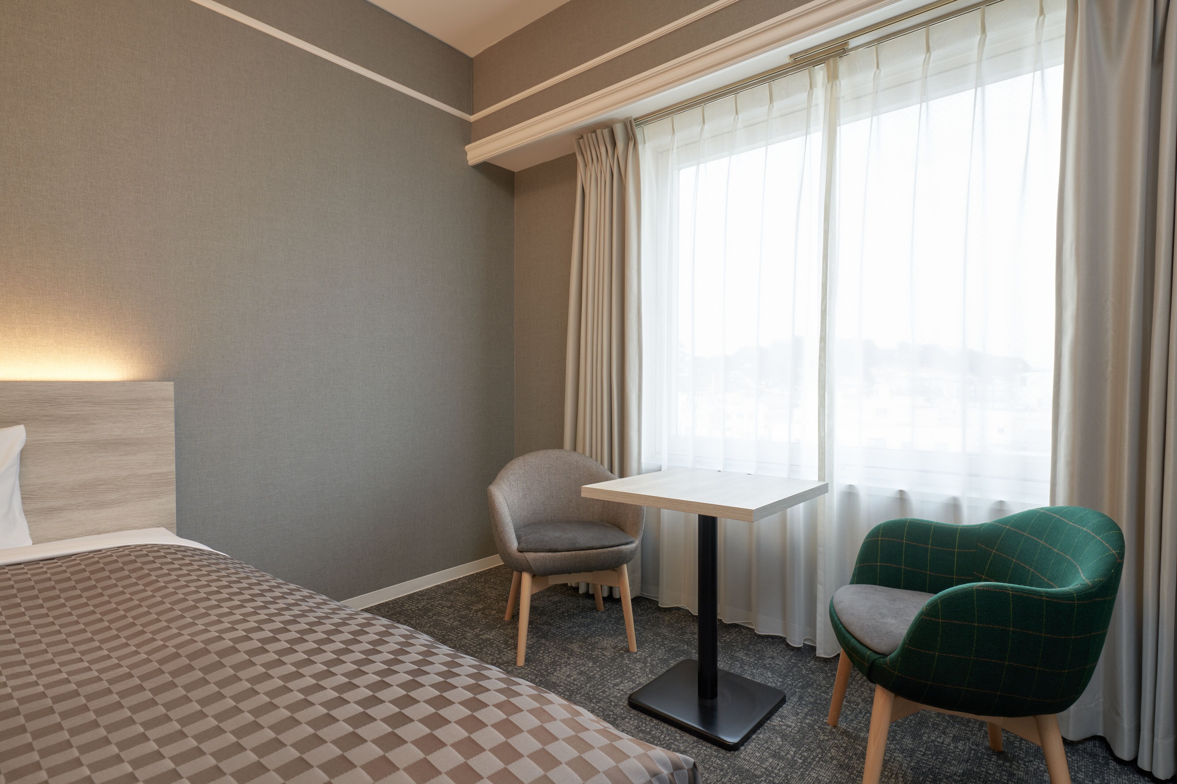 Habitación de hotel con cama, una mesita, dos sillas y una ventana con cortinas.