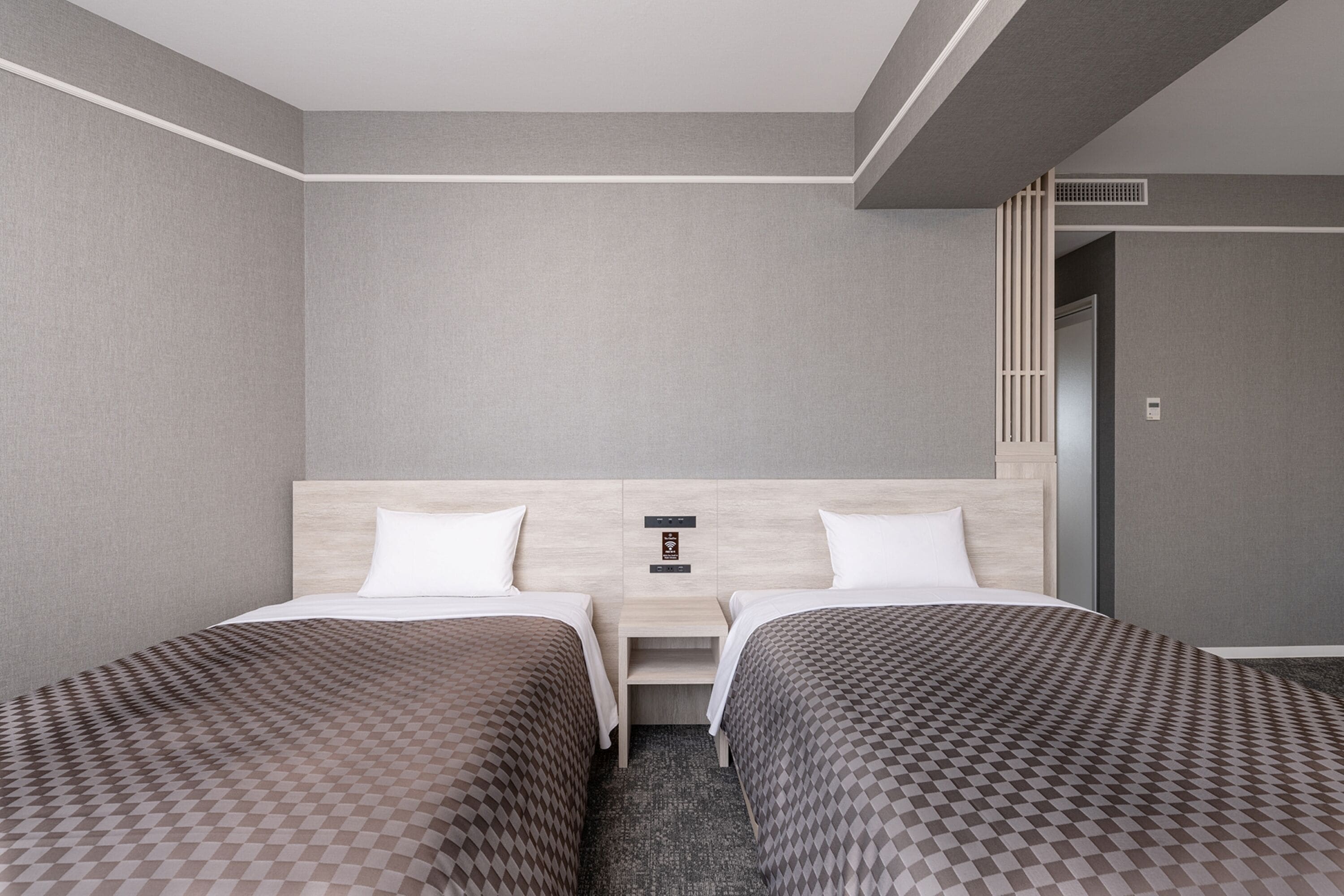 Ein Hotelzimmer mit zwei Betten, einem Holzkopfstück, einem kleinen Tisch und einer wandmontierten Steuerung.