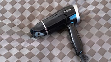 Un sèche-cheveux avec un cordon et une multiprise posés sur une surface en tissu à carreaux.