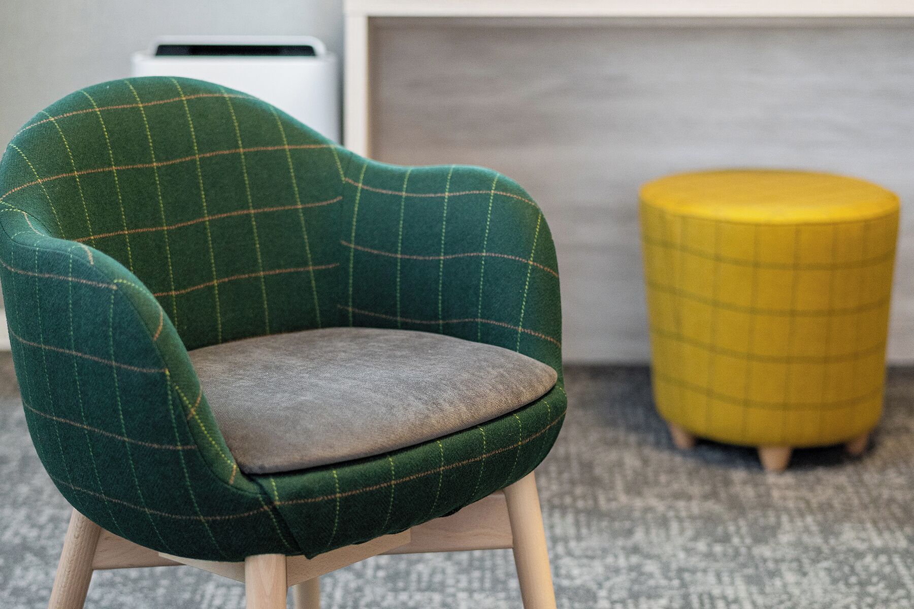 A green armchair with a plaid pattern and a wooden base, positioned next to a yellow ottoman with a grid design.
