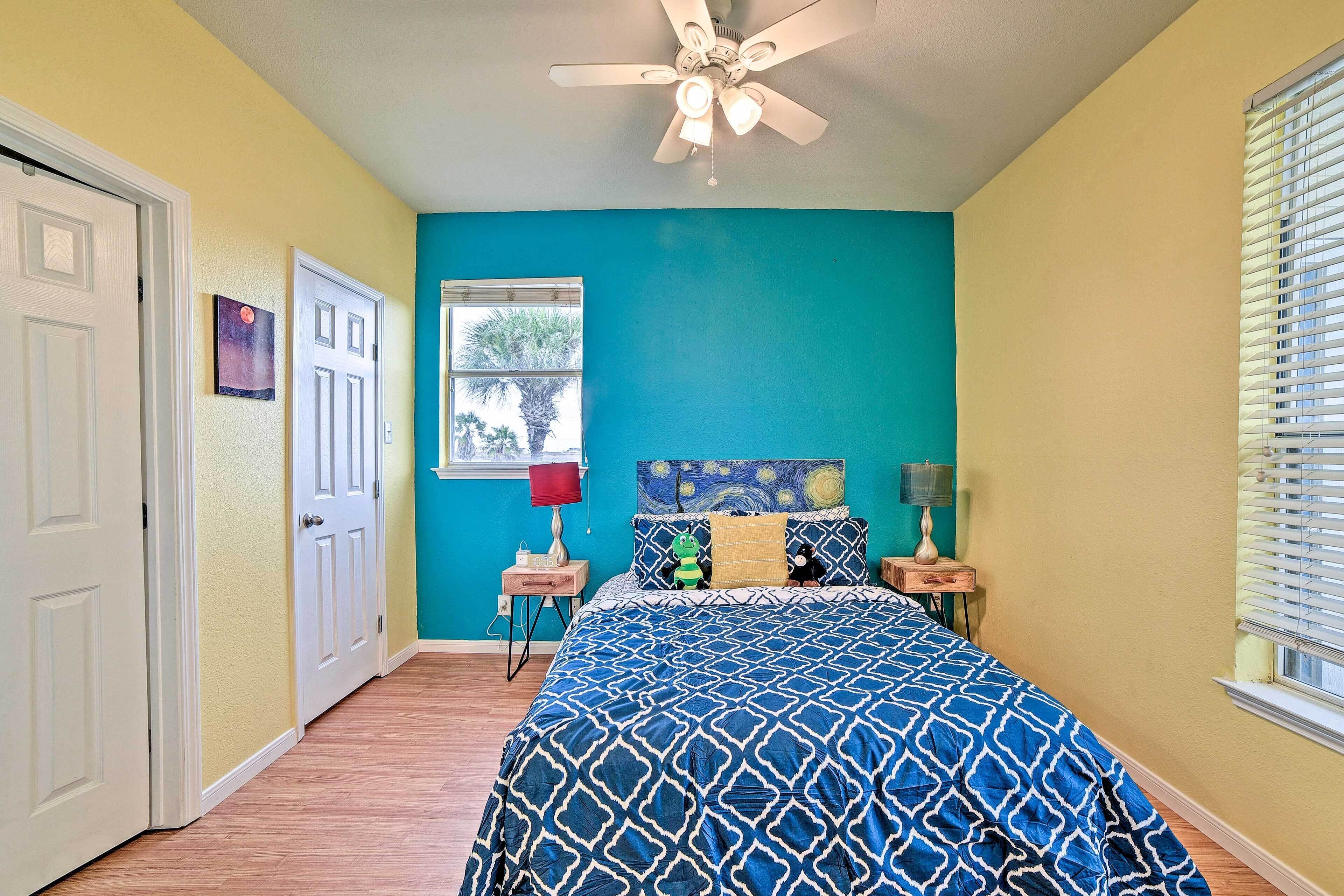 A bedroom with a bed, a ceiling fan, a window with blinds, and a door.