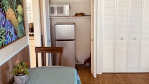Et spiseområde med et bord og stole, en mikrobølgeovn, et køleskab og et sæt hvide, persiennelugede skabe.
