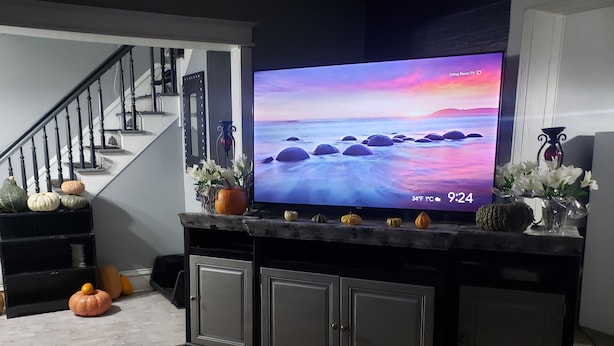 Una sala de estar con un televisor sobre un mueble de entretenimiento negro, una escalera y calabazas decorativas.