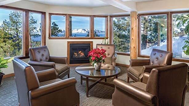 A cozy room with leather chairs, a round table, and a fireplace. Large windows offer a view of mountains and trees.