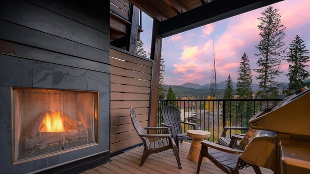 A wooden deck with a fireplace, outdoor seating, and a scenic mountain view.