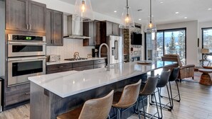A modern kitchen with stainless steel appliances, a large island with bar stools, and pendant lighting.