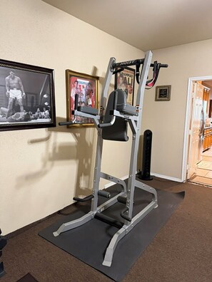 Ein Heimfitnessraum mit einer Gewichtbank, einer Klimmzugstange und einem an der Wand befestigten Trainingsgerät.