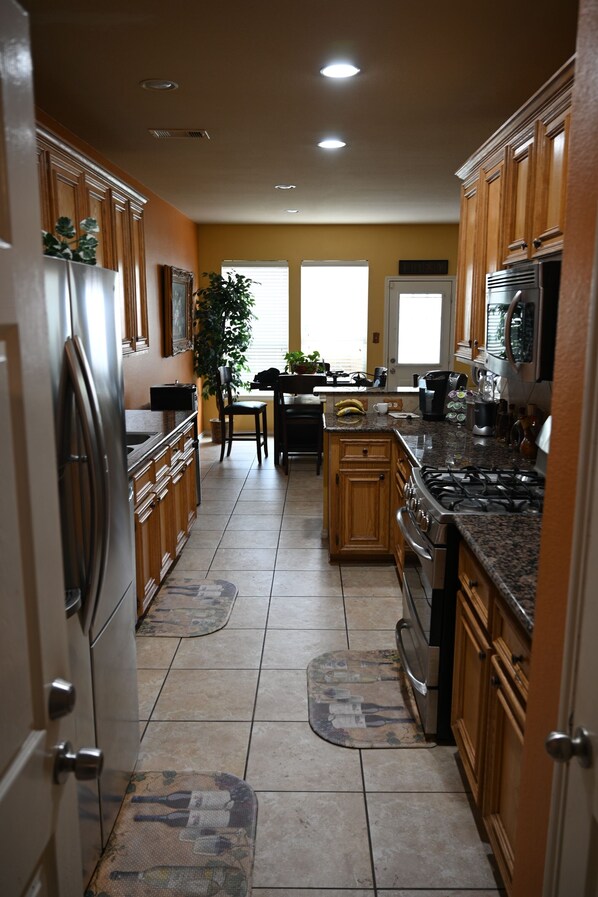 A kitchen with wooden cabinets, a stainless steel refrigerator, a gas stove, and a dining area with a table and chairs.