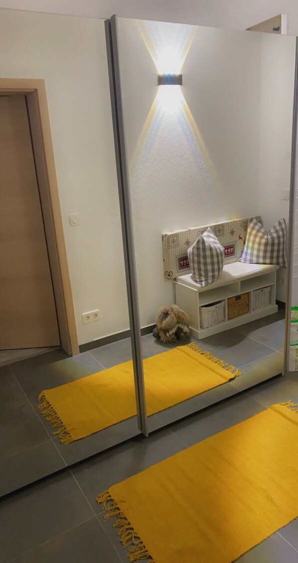 A room with a large mirror, a small dog, a yellow rug, and a white cabinet with checkered pillows. - Apartment and studio Weißensee (Füssen)