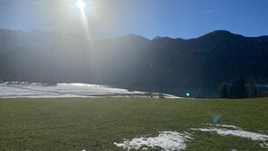 A grassy field with snow patches and mountains in the background. - Apartment and studio Weißensee (Füssen)