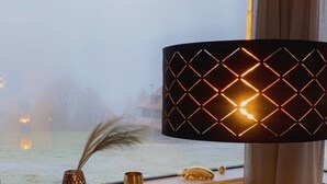 A room with a large window, a round wooden table, and a decorative lamp. - Apartment and studio Weißensee (Füssen)