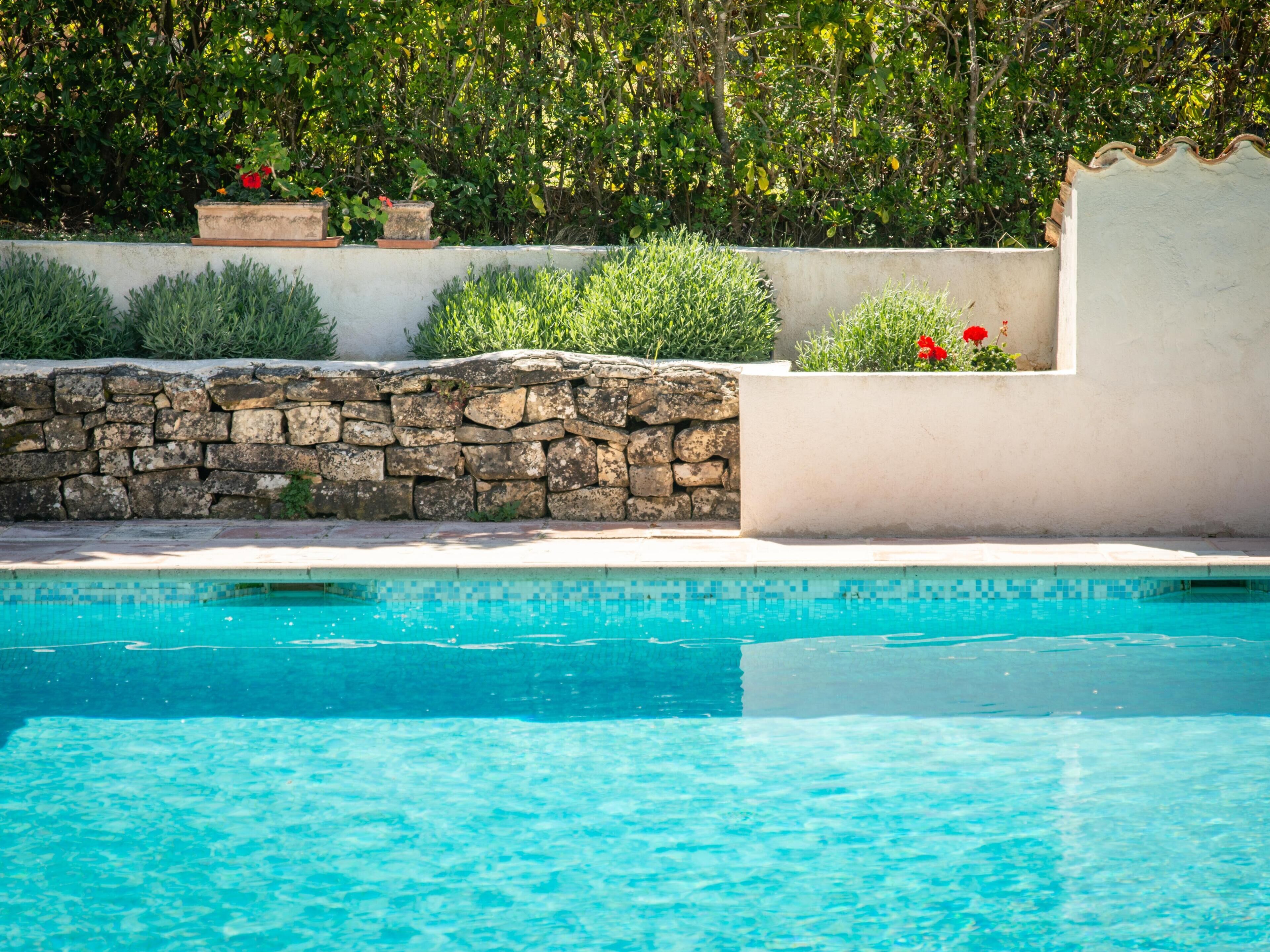 A swimming pool with a stone wall and greenery in the background.
