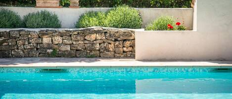 A swimming pool with a stone wall and greenery in the background.