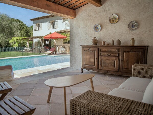 A poolside area with a wooden bench, wicker furniture, and a dining table.