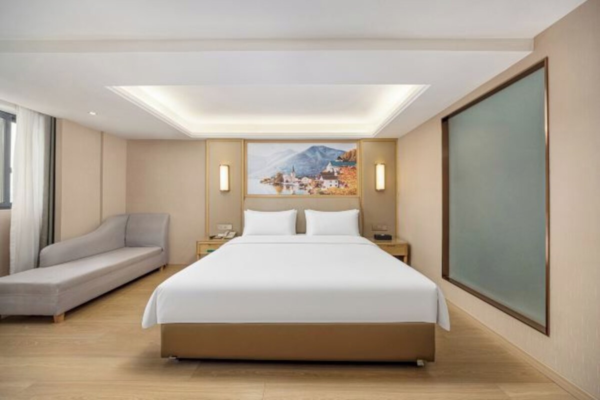 A hotel room with a large bed, a sofa, a nightstand, and a painting on the wall.