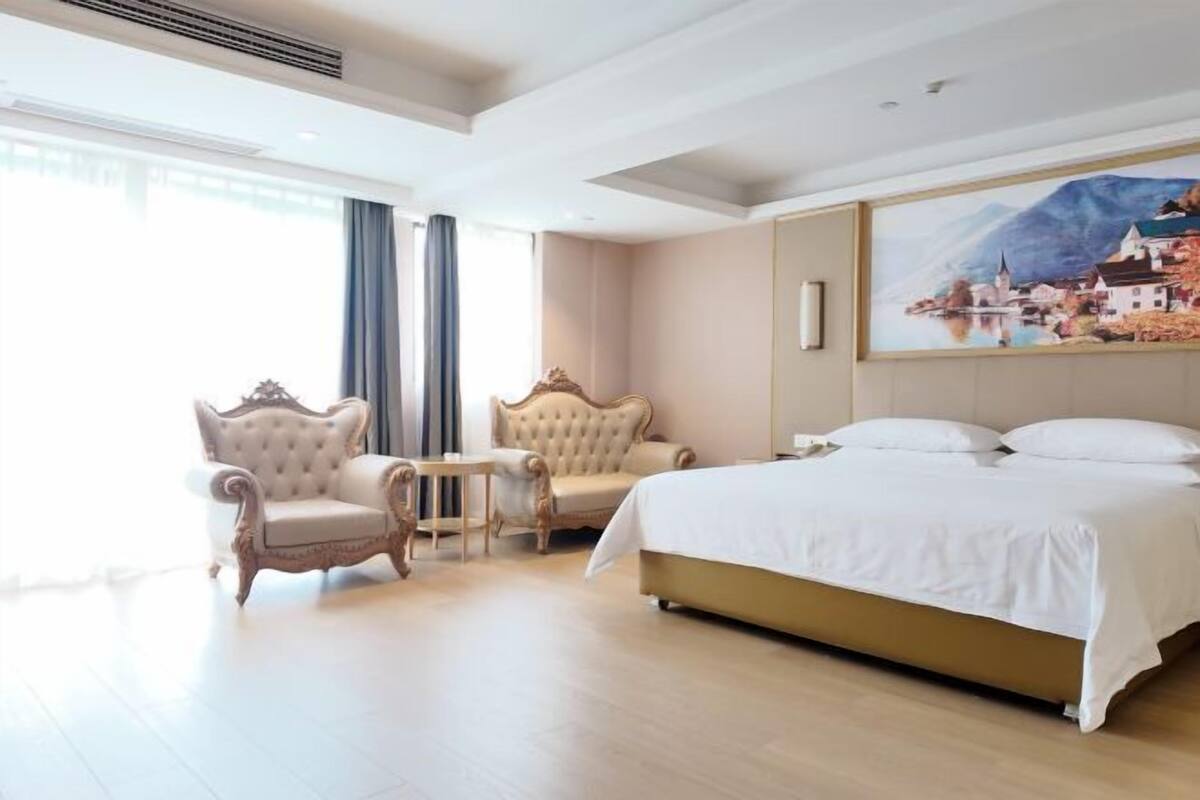 Ein Hotelzimmer mit einem großen Bett, zwei Sesseln, einem kleinen Tisch und einem Gemälde an der Wand.