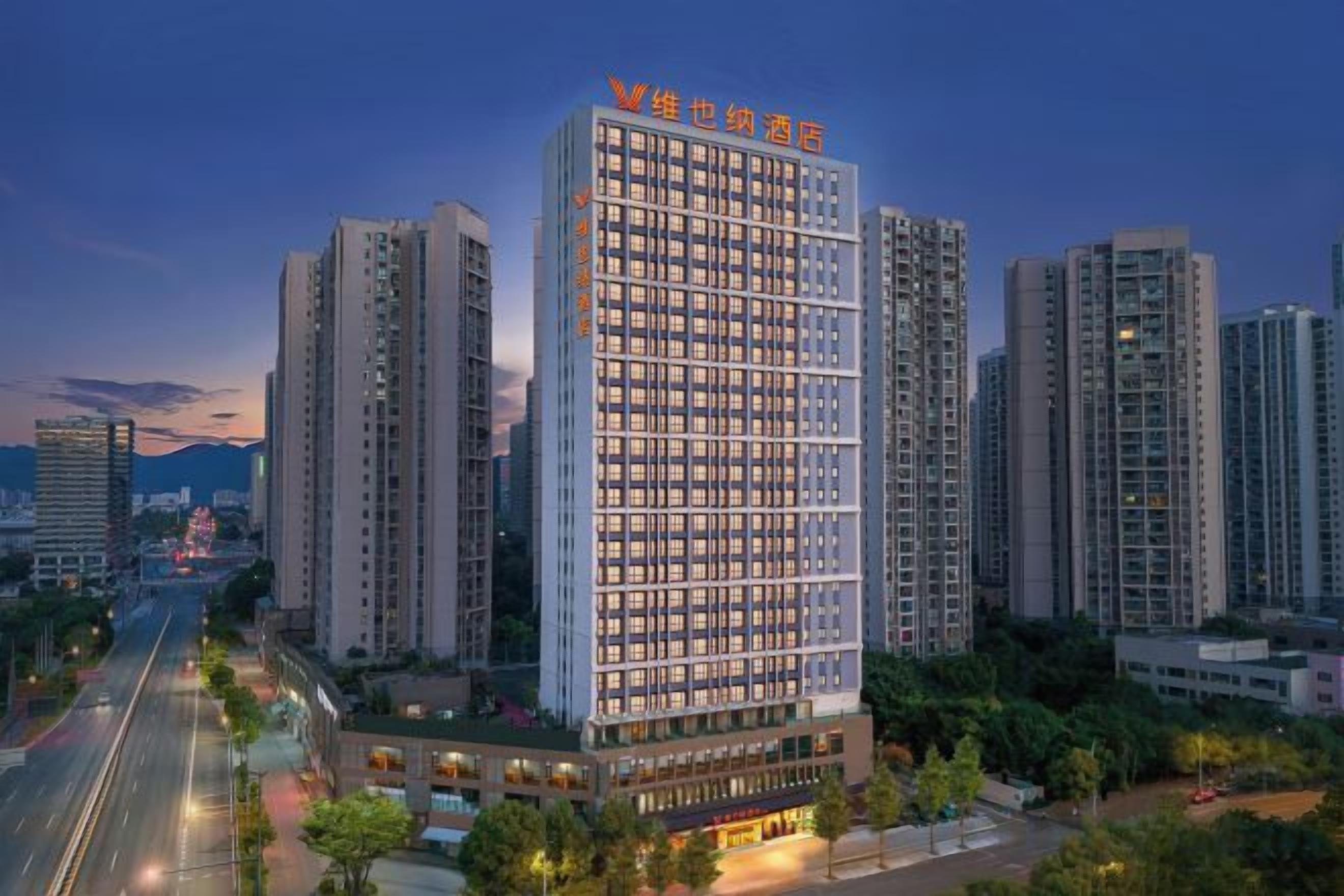 A high-rise hotel with multiple floors, surrounded by other buildings, and a road in the foreground.