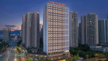 A high-rise hotel with multiple floors, surrounded by other buildings, and a road in the foreground.