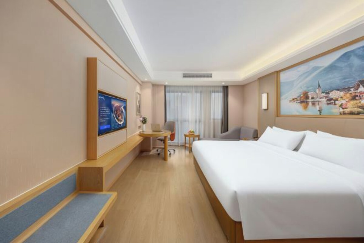 A hotel room with a bed, desk, chair, and a television.
