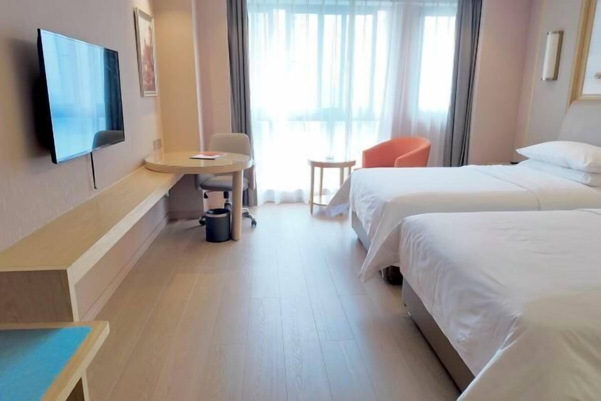 Ein Hotelzimmer mit Bett, Schreibtisch, Stuhl, Fernseher und einem Fenster mit Vorhängen.
