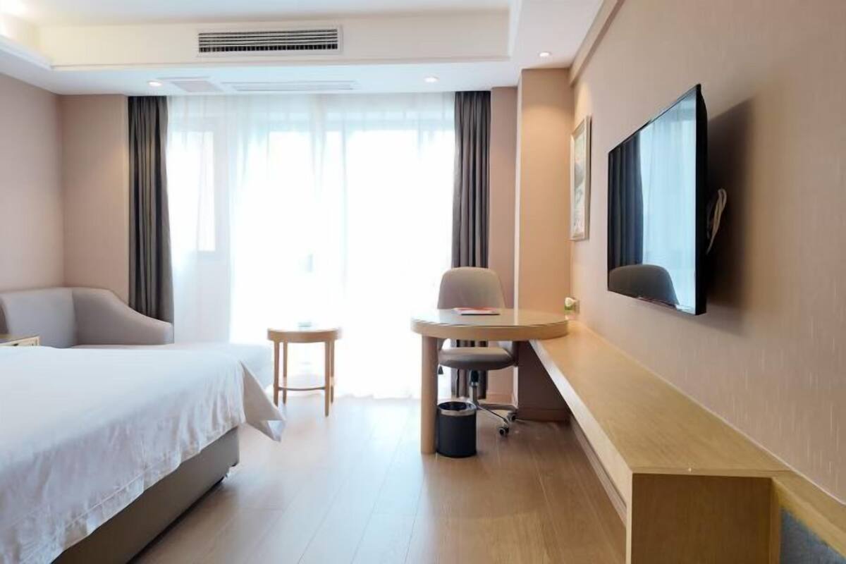 Ein Hotelzimmer mit Bett, Schreibtisch, Stuhl, Fernseher und einem Fenster mit Vorhängen.