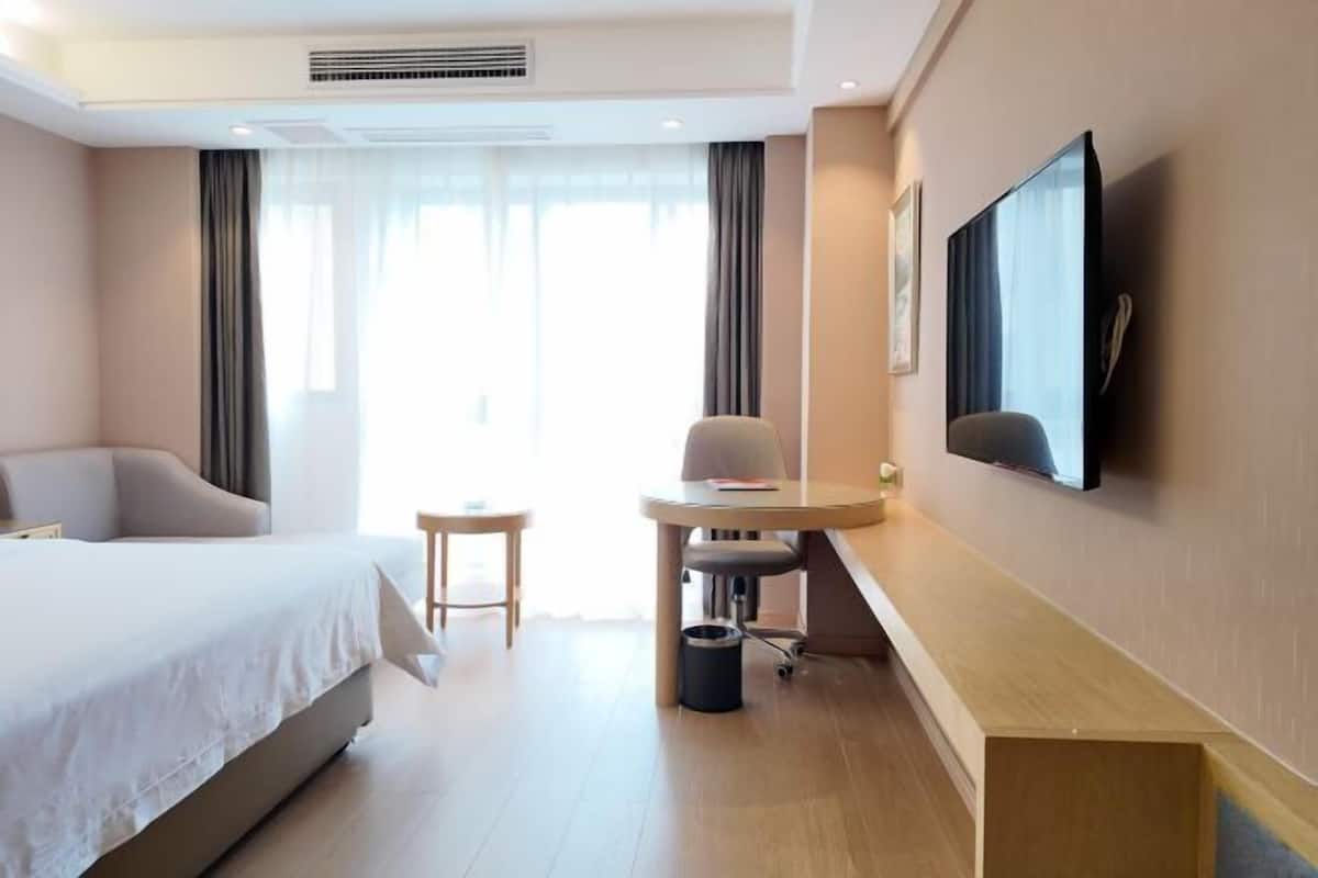 A hotel room with a bed, a desk, a chair, a TV, and a window with curtains.