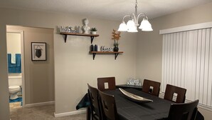 Een eetruimte met een tafel voor vier personen, omringd door stoelen, een kroonluchter en decoratieve items op planken.