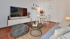 A modern living room with a flat-screen TV, a round coffee table with a bottle and glasses, a grey sofa, and a dining area with a white table and chairs. - Adumar - Javea, Costa Blanca (Javea)