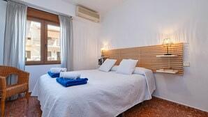 A hotel room with a bed, a chair, a window with curtains, a wall-mounted shelf, and an air conditioning unit. - Adumar - Javea, Costa Blanca (Javea)