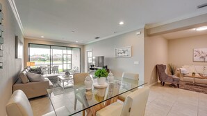 Ampla sala de estar com mesa de jantar de vidro, sofá e mesa de centro. Há uma TV e uma planta no ambiente.