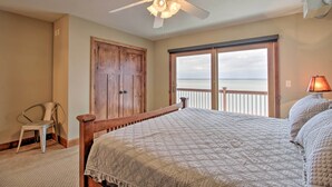 Un dormitorio con una cama grande, un ventilador de techo, un armario de madera y vistas al océano a través de un ventanal.