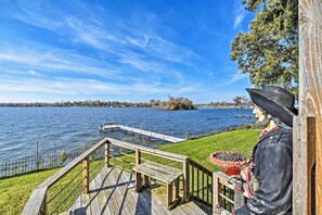 A wooden deck with a bench overlooking a lake, a statue of a historical figure, and a distant shoreline with boats.