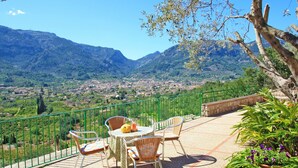 Una terrazza con tavolo e sedie, vista su una valle e montagne sullo sfondo.