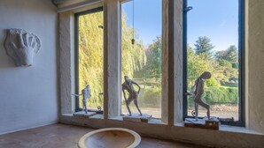Una stanza con ampie finestre, pavimento in legno e tre sculture esposte su piedistalli.