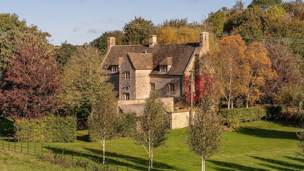 A stone house with multiple chimneys, surrounded by trees and a well-maintained lawn.