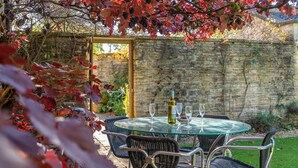 Zona pranzo all'aperto con tavolo rotondo in vetro, sedie in metallo e una bottiglia di vino.