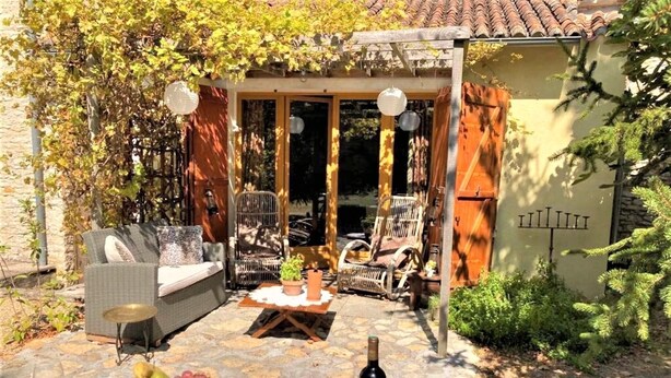 Un área de comedor al aire libre con mobiliario de mimbre, una mesa dispuesta para una comida y una botella de vino.