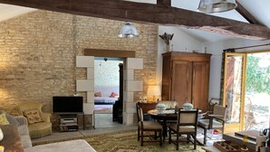 Una sala de estar acogedora con una pared de piedra, vigas de madera, un televisor, un sofá, una mesa de comedor con sillas y un ventanal grande.